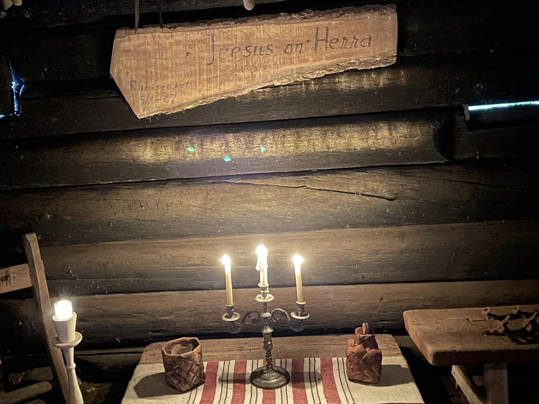 kuvassa vanha hirsiseinä, jossa teksti Jeesus on Herra ja edessä kynttelikkö